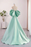 Mint green evening gown with a large bow on a mannequin against a light pink wall.