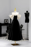 Black evening gown with white bow on a mannequin against a gray wall.