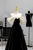 Black evening gown with a large white bow on a mannequin against a gray background.