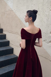Woman in a burgundy velvet dress standing on steps against a textured wall.