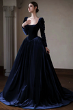 Woman wearing a dark blue velvet gown standing indoors against a neutral wall.