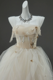 Elegant beige evening gown with floral embellishments on a mannequin against a dark background
