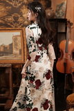 Woman in a floral dress standing in an interior setting with a painting and cello in the background