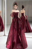 Woman in a burgundy evening gown standing in front of a mirror.