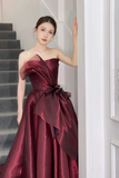 Woman in a burgundy strapless gown standing on a staircase.