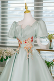 Light green dress with floral embellishments on a mannequin against a window background.