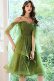 Woman wearing a green dress with sheer sleeves in front of a window with greenery outside.