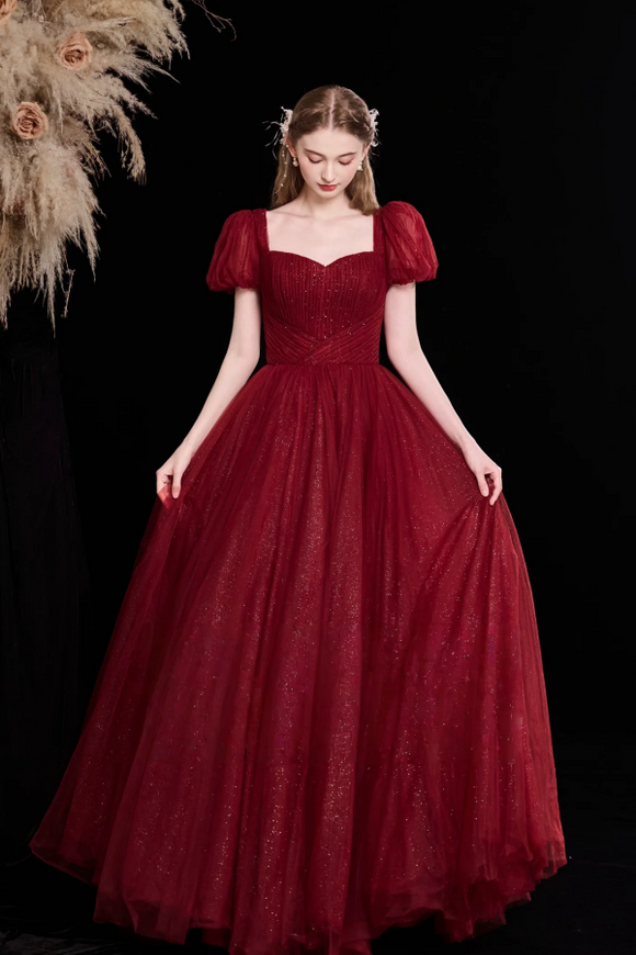 Woman wearing a burgundy evening gown with puff sleeves against a black background