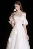 Woman in a white wedding dress with heart details holding a rose against a black background