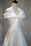 White off-shoulder dress with a large bow on a mannequin against a neutral background