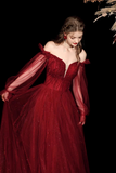 Woman in a red off-shoulder gown with sheer sleeves against a dark background