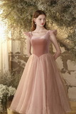 Woman in a pink dress standing in a garden with flowers and a building in the background
