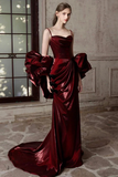 Woman wearing a burgundy evening gown with large bow detail in an elegant indoor setting.