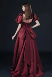 Woman wearing a burgundy evening gown with a large bow detail on a dark background