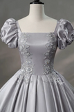 Gray evening gown with floral embellishments on a mannequin against a gray background