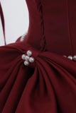 Close-up of a burgundy dress with pearl details on a white background