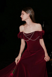 Woman in a burgundy off-shoulder dress with pearl details against a dark background