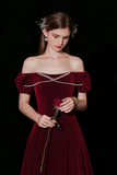 Woman in a burgundy off-shoulder dress holding a rose against a black background