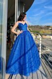 Woman in a blue sparkly dress standing on a balcony with a clear sky background