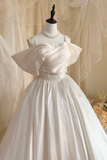 White wedding dress with a large bow on a mannequin against a beige curtain.