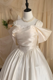 White wedding dress with a large bow on a mannequin against a beige curtain.