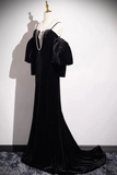 Black evening gown with pearl necklace on a mannequin against a white wall.