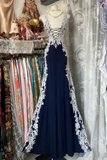 Navy blue evening gown with white lace details on a mannequin against a clothing store background.