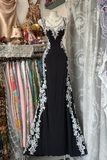 Black evening gown with white lace details on a mannequin against a background of colorful fabrics.