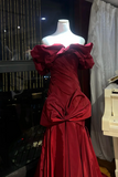 Red evening gown on a mannequin in a room with a piano and curtains.