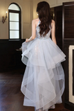 Woman in a white evening gown standing in an elegant room with wooden floors and a large mirror.