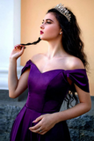 Woman wearing a purple off-shoulder dress with a bow detail, holding a black ribbon.