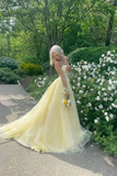 Woman in a yellow dress standing outdoors with greenery and flowers in the background