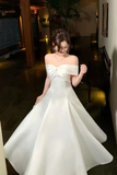 Woman in a white off-shoulder dress standing indoors.