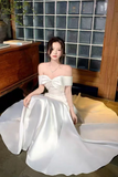 Woman in a white off-shoulder dress sitting on a couch in a room with glass block walls.