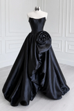 Black strapless gown with a large floral detail on a mannequin against a white wall.