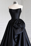 Black evening gown with a large floral bow on a mannequin against a white paneled wall.