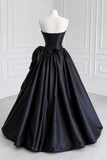 Black strapless gown on a mannequin against a white paneled wall.
