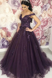A woman wearing a dark purple off-the-shoulder ball gown with floral lace applique and a full tulle skirt, standing in front of a pink and white rose wallpaper.