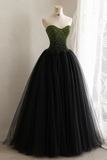 A strapless ball gown displayed on a mannequin, featuring a green beaded sweetheart bodice and a voluminous black tulle skirt.