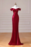 A floor-length off-the-shoulder evening gown in deep burgundy red, displayed on a white mannequin dress form against a light beige paneled wall and wood floor.