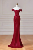 A floor-length off-the-shoulder evening gown in deep burgundy red, displayed on a white mannequin dress form against a light beige paneled wall and wooden floor.