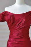 A close-up of a deep red off-the-shoulder dress with ruched draping on a white mannequin torso against a neutral gray background.