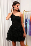 A woman modeling a short black one-shoulder lace dress with sequined details and a tiered skirt, standing in front of white curtains with a gold clothing rack visible in the background.