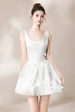 A woman modeling a sleeveless white satin dress with a square neckline and a flared skirt, set against a soft beige studio background.