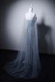 A strapless light blue tulle gown with a long sheer overlay and beaded vertical detailing, displayed on a white mannequin against a dark gray studio wall.