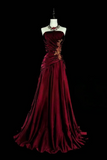 A floor-length burgundy evening gown displayed on a white mannequin against a solid black background. The strapless gown features a ruched bodice with gold floral embroidery and a draped satin skirt.