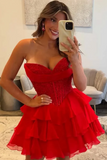 A woman takes a mirror selfie wearing a bright red strapless sweetheart prom dress with a beaded corset-style bodice and a tiered ruffled skirt, standing in a modern living room.