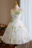 A sleeveless white tulle dress with green floral embroidery and 3D flower appliqués on the bodice and waist, displayed on a mannequin in an indoor setting.