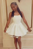 A young girl wearing a short white sleeveless dress with a structured bodice and flared skirt, standing indoors against a cream-colored wall with gold trim.