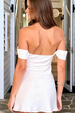 A woman viewed from behind wearing a white off-the-shoulder mini dress with a scoop back, standing in front of a doorway.